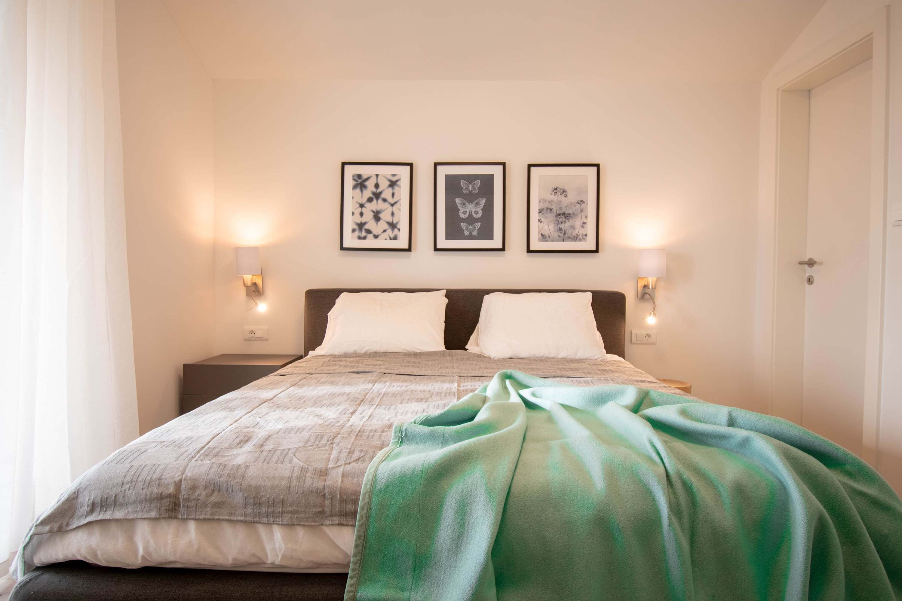A neatly made bed with a green blanket, two bedside tables with lamps, and three framed pictures on the wall.