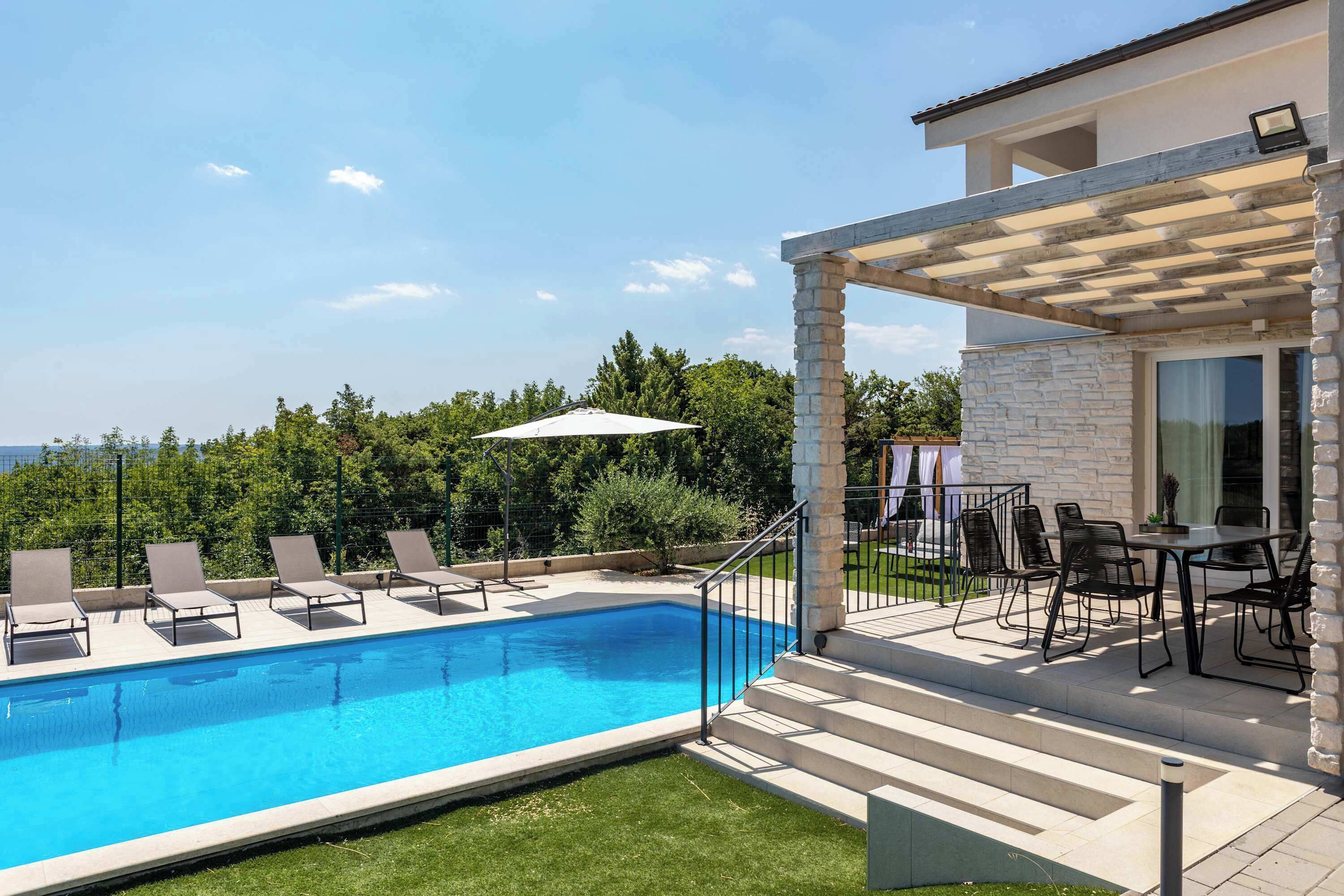 A swimming pool with lounge chairs, a covered patio with outdoor furniture, and a stone wall.