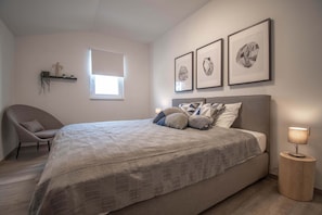 A bedroom with a bed, a chair, a bedside table with a lamp, a window, and wall-mounted artwork. - Villa Adriatica (Sveti Lovrec Labinski)