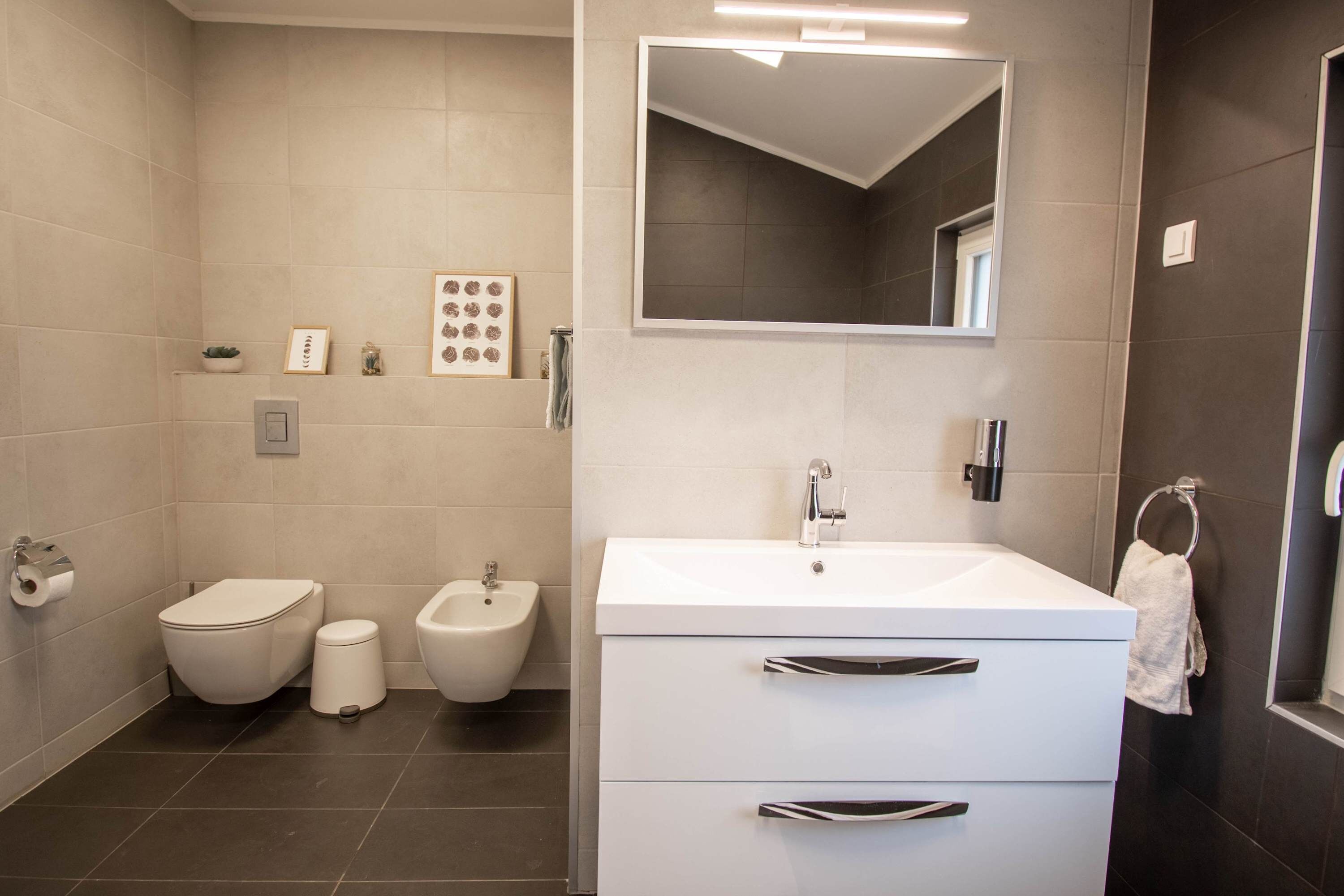A modern bathroom with a white sink, bidet, and toilet.