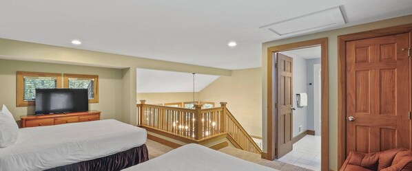 Un dormitorio con dos camas, un televisor sobre una mesita de noche, una escalera de madera y una puerta que da a otra habitación.
