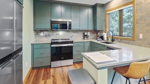 Cozinha moderna com armários verde-água, eletrodomésticos de aço inoxidável e uma ilha grande com banquetas.