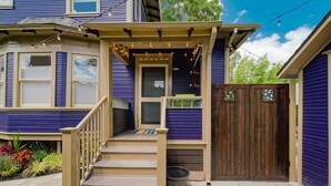 A two-story house with a porch, a wooden gate, and a stone pathway. - Patio Villa: sleeps 1–4; 2 kitchens; gas fire pit (Portland)