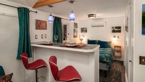 A compact room with a kitchenette, a bed with a blue and green patterned bedspread, and a red chair. - Patio Villa: sleeps 1–4; 2 kitchens; gas fire pit (Portland)