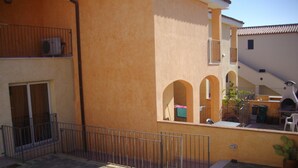 A courtyard with a paved area, a metal fence, and a building with a beige facade. - Tommy House - Convenient, functional and comfortable home (Orosei)