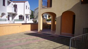 A courtyard with tiled flooring, white buildings with balconies, and a metal railing. - Tommy House - Convenient, functional and comfortable home (Orosei)