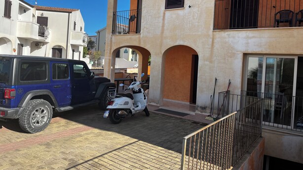 A residential building with a balcony, a parked scooter, and a blue SUV. - Tommy House - Convenient, functional and comfortable home (Orosei)