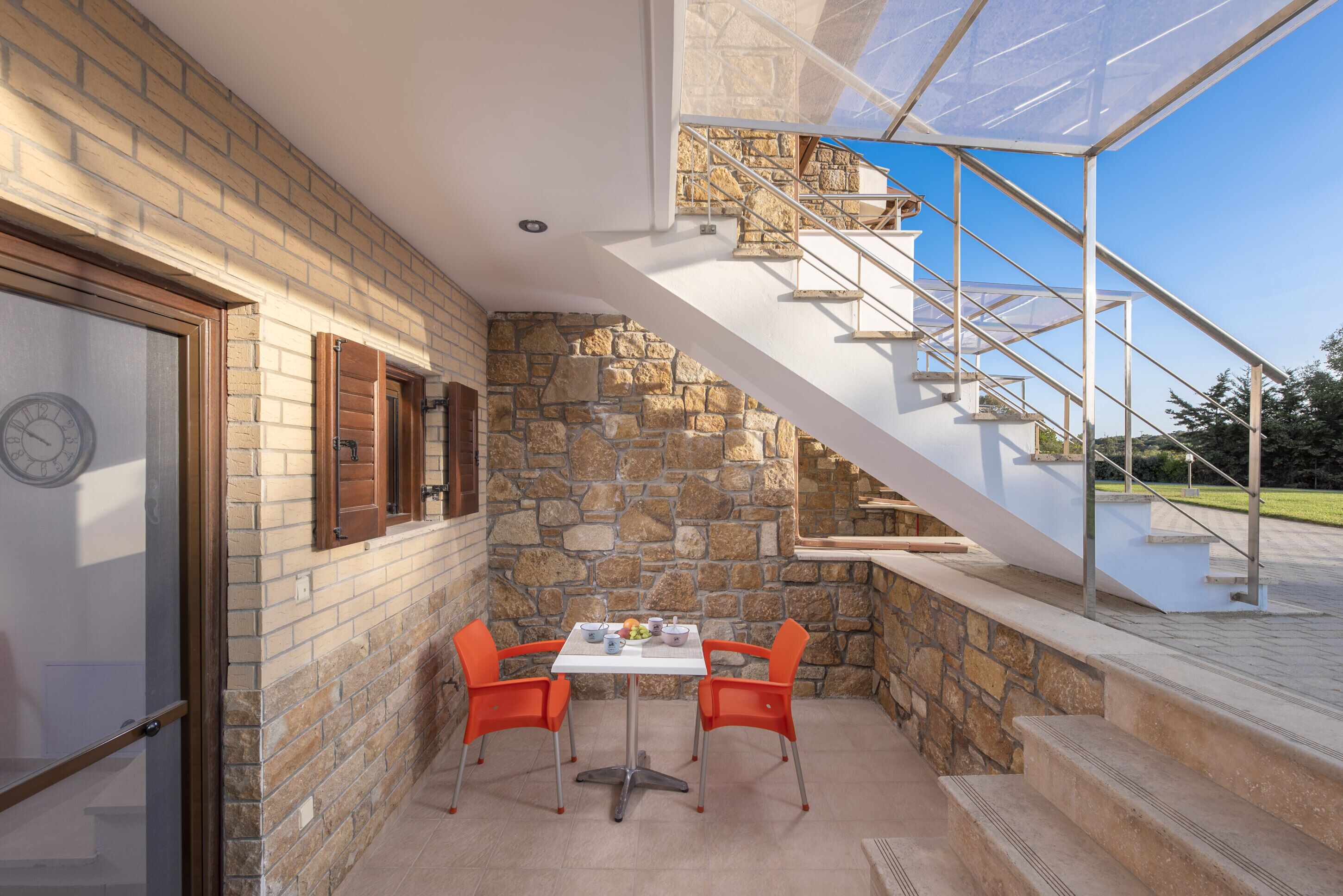 A patio with a stone wall, a table with chairs, and a staircase with a glass enclosure.