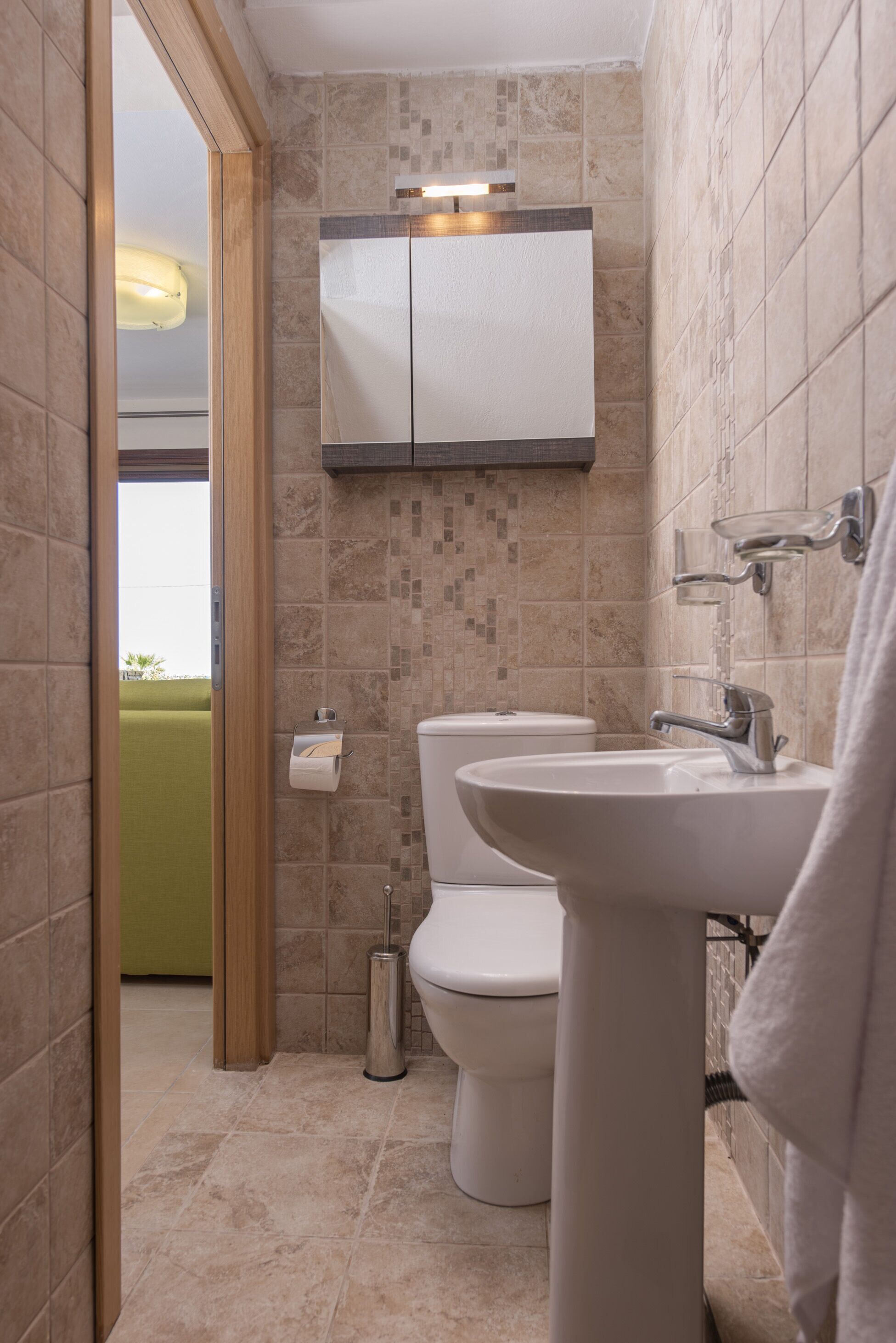 Un baño con inodoro, lavamanos y un armario sobre el lavamanos.