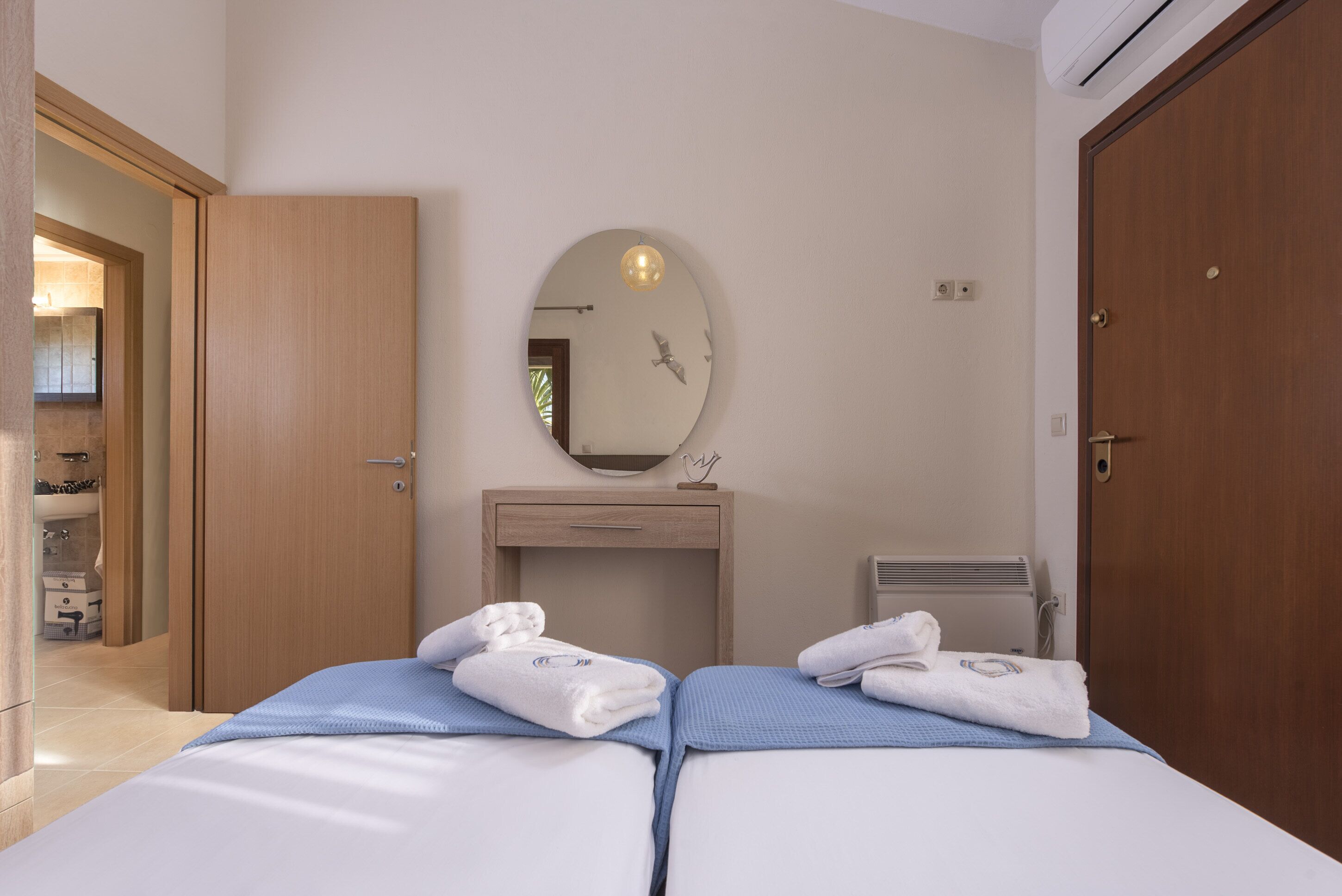 A hotel room with two beds, a wooden wardrobe, a mirror, and a radiator.