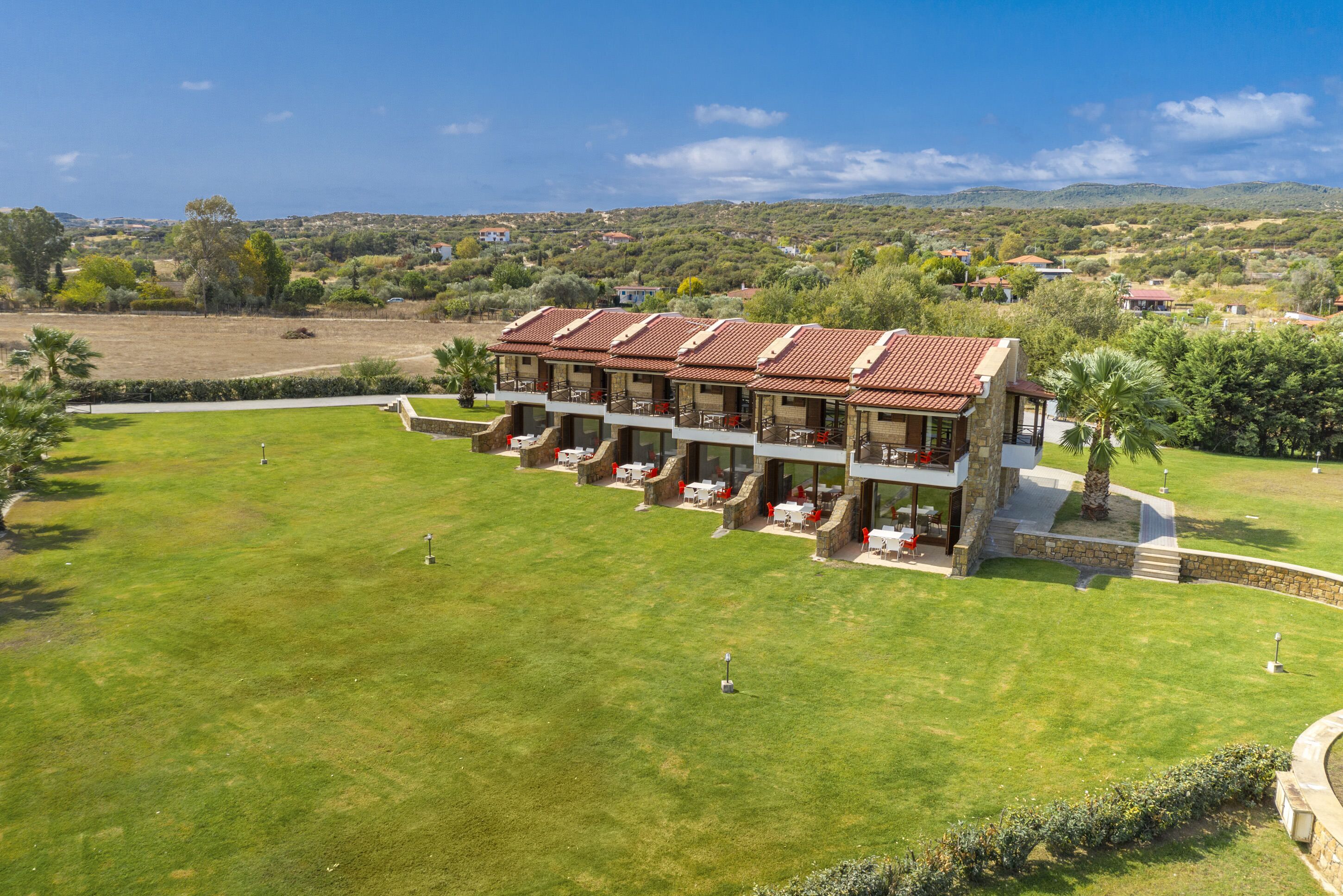 A hotel with multiple balconies, a well-maintained lawn, and a view of the surrounding countryside.