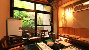 A room with a wooden sofa, a dining table with chairs, a refrigerator, and a large window with a view of greenery. - Yamashita (Kanazawa)