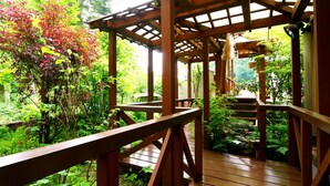 A wooden deck with a pergola structure, surrounded by lush greenery and a small pond. - Yamashita (Kanazawa)