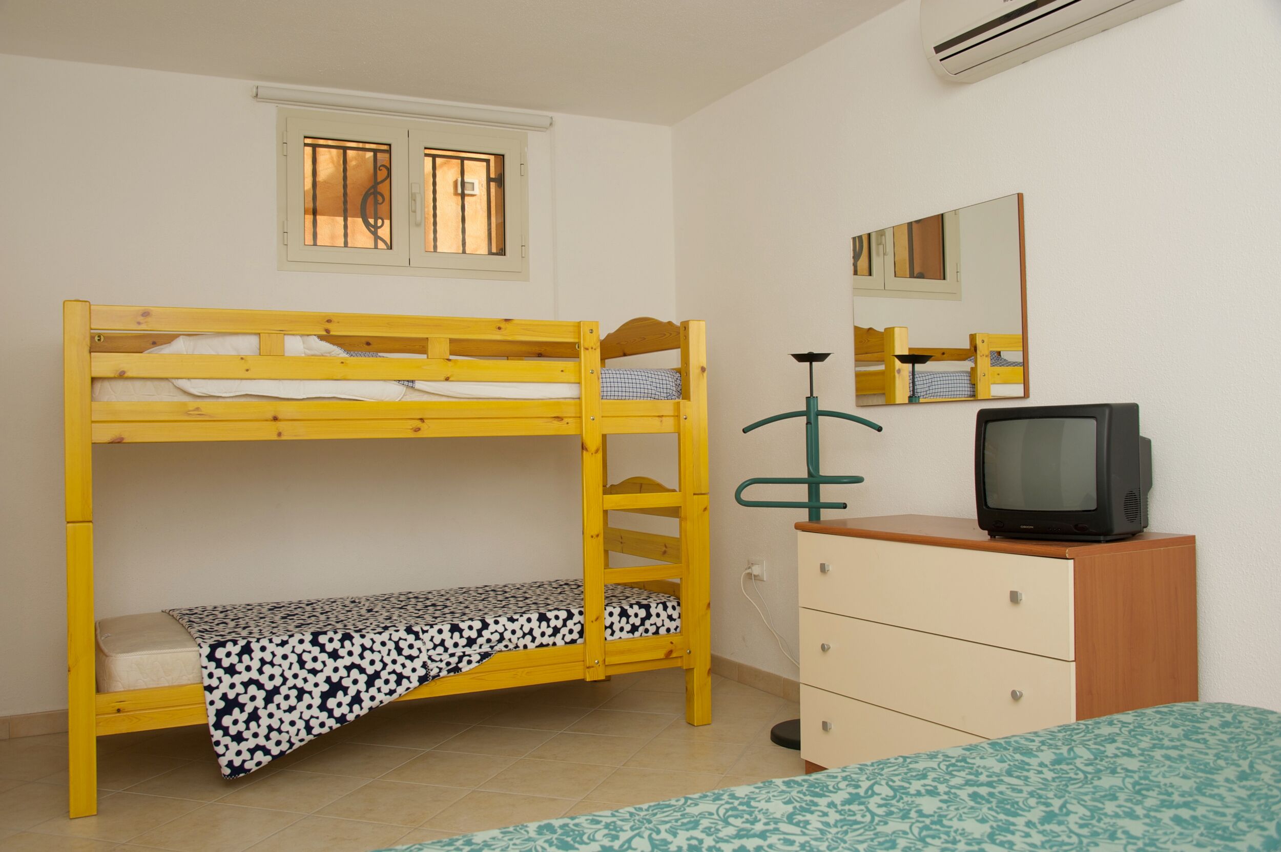 Una cama litera con una cama inferior, un aparador, un televisor y una ventana con barrotes.