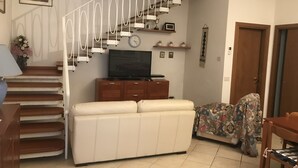 A living room with a staircase, a sofa, a television, and a patterned chair. - Small villa in a great location (Viareggio)