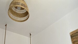 A bedroom with a bed, a hanging light fixture, a mirror, and a wall-mounted rack with clothes.
