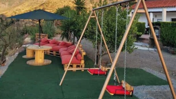 A patio with a swing set, red cushioned seating, and a view of a mountain.