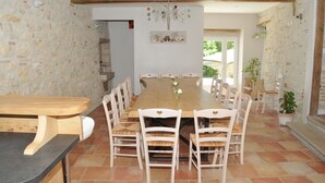 Un espace repas avec une longue table en bois, des chaises blanches et un lustre.