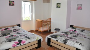 Une chambre avec deux lits, un berceau en bois et un petit tabouret.