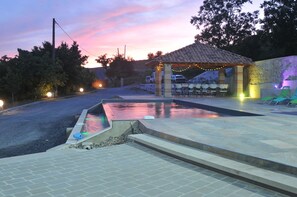 Ein Außenpoolbereich mit einer Pergola, Stühlen und einer kleinen Bühne mit Lichterketten.