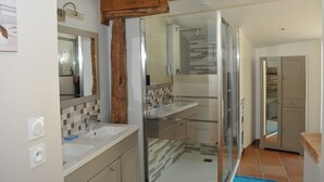 Une salle de bain moderne avec une douche à parois de verre, un grand miroir et une poutre en bois au plafond.