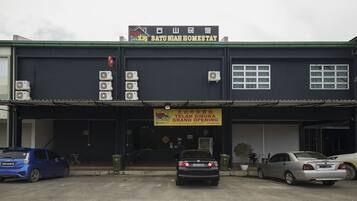 A building with a sign reading "Batu Mihah Homestay" and another sign indicating a grand opening. There are three cars parked in front.