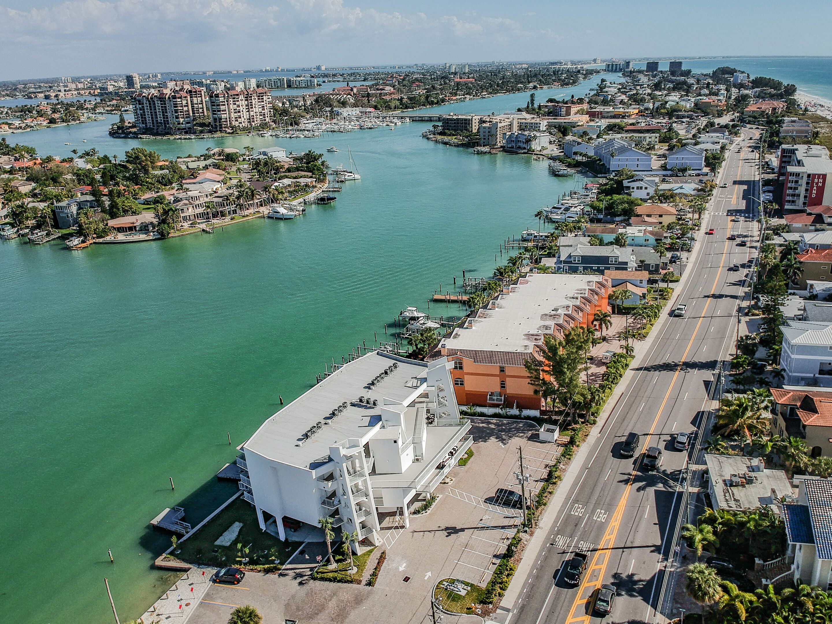 An aerial view of a coastal city with a marina, buildings, and a road.