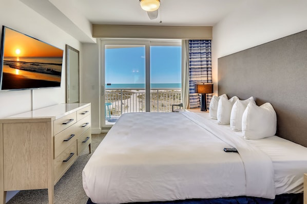 A hotel room with a large bed, a desk, and a TV on the wall.