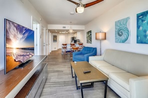 A modern living room with a flat-screen TV, a wooden coffee table, a beige sofa, and a blue armchair.