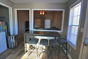 A compact kitchen with a central island, bar stools, and a window with blinds.