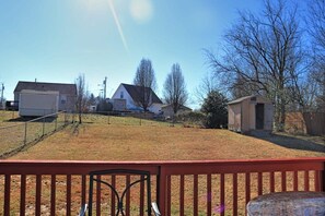 Un jardin à l’arrière d’une maison, avec une zone délimitée par une clôture, un petit abri de jardin et des maisons en arrière-plan.