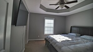 Une chambre dotée d’un ventilateur de plafond, d’un lit, d’une fenêtre avec des stores et d’un téléviseur fixé au mur.