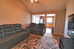 A living room with a sofa, two recliners, a rug, and a TV.