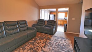 Un salon avec un canapé, deux fauteuils, un tapis et un téléviseur.