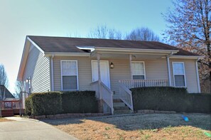 A two-story residential house with a front porch, a visible staircase, and a well-maintained lawn.