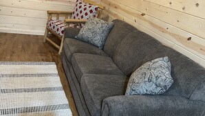 Een gezellige kamer met een grijze bank, gestreepte kussens, een geweven vloerkleed en houten wanden.