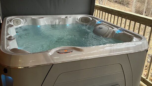 Een hottub op een houten terras met uitzicht op een bos.
