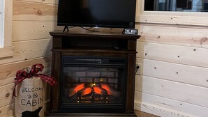 Interieur van een houten chalet met een televisie op een standaard boven een open haard, een welkomstpakket en een raam met uitzicht op het plafond.