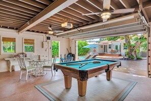 A pool table in a covered area with a ceiling fan, a table with chairs, and a view of a pool and outdoor seating area. - Steps from Beach / Quaint Cottage / Heated Pool / Sand Key / RESlDENCES (Fort Lauderdale)
