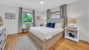 A bedroom with a wooden bed, a bedside table with a lamp, and a window with curtains.