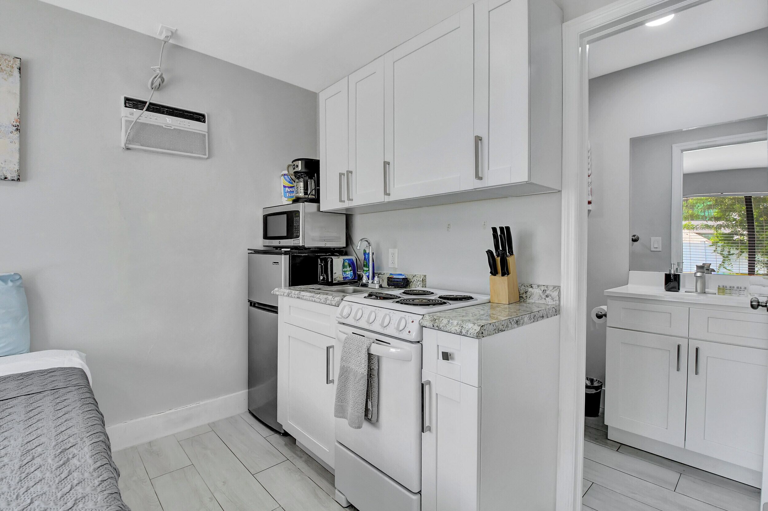 Une cuisine de taille réduite avec des meubles blancs, un four à micro-ondes, une cuisinière et un évier.