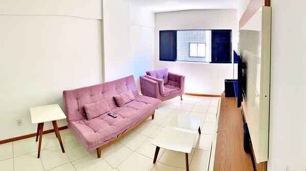 Una sala de estar moderna con un sofá rosa, una mesa de centro blanca y un mueble para la televisión.