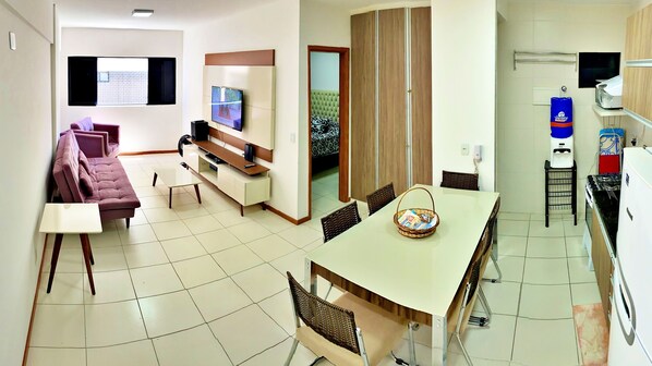 Una sala de estar moderna con sofá, televisor y comedor con sillas y una mesa.