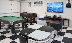 A pool table, foosball table, and a television in a room with a checkered floor.