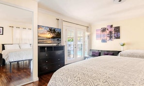 A bedroom with a bed, a dresser, a TV, and a view of the outdoors.