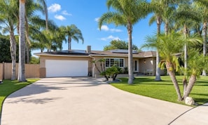 A single-story house with a garage, surrounded by palm trees and a well-maintained lawn.