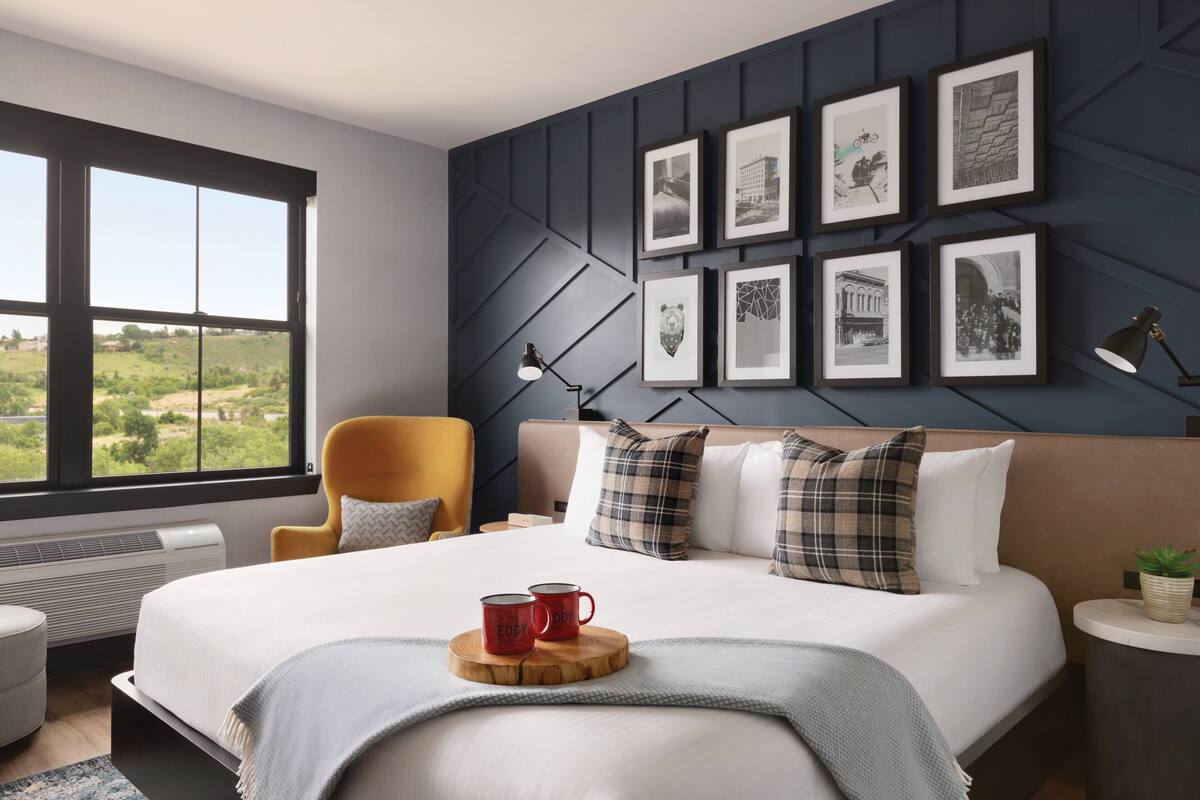 A modern hotel room with a large bed, a view of the outdoors, and a wall decorated with framed pictures.