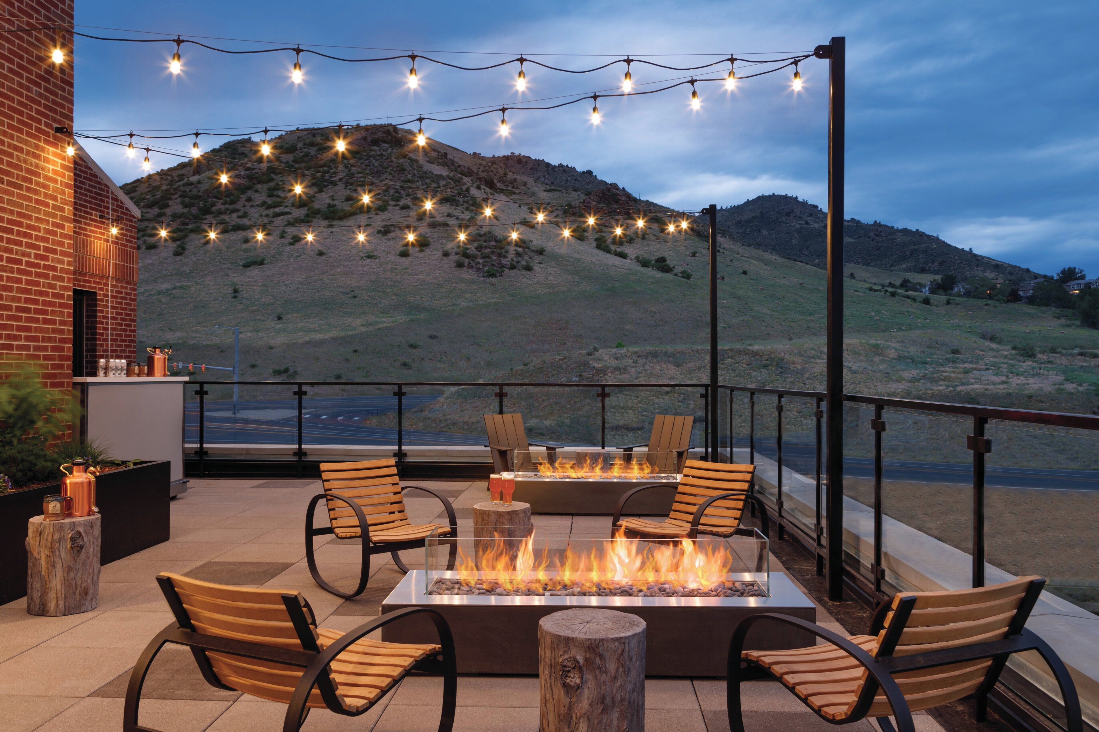An outdoor patio with a fire pit, seating, and string lights against a backdrop of a hilly landscape.