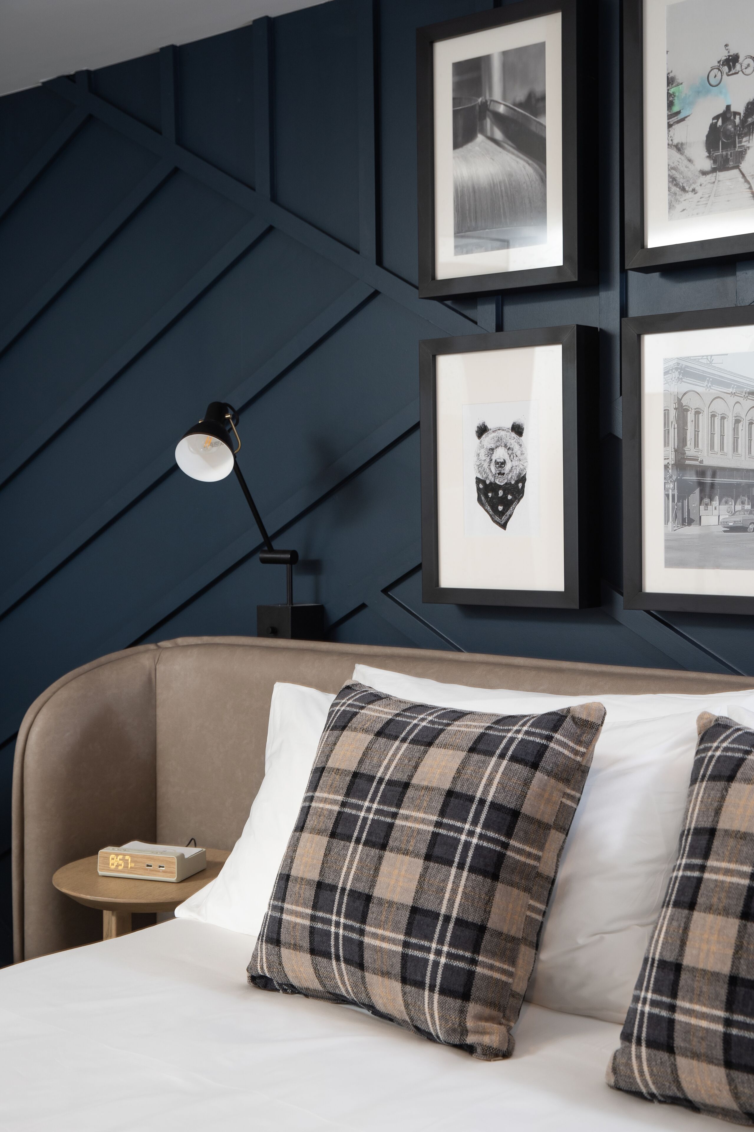 Una cama bien hecha con almohadas a cuadros, una mesita de noche con lámpara y cuadros en la pared.
