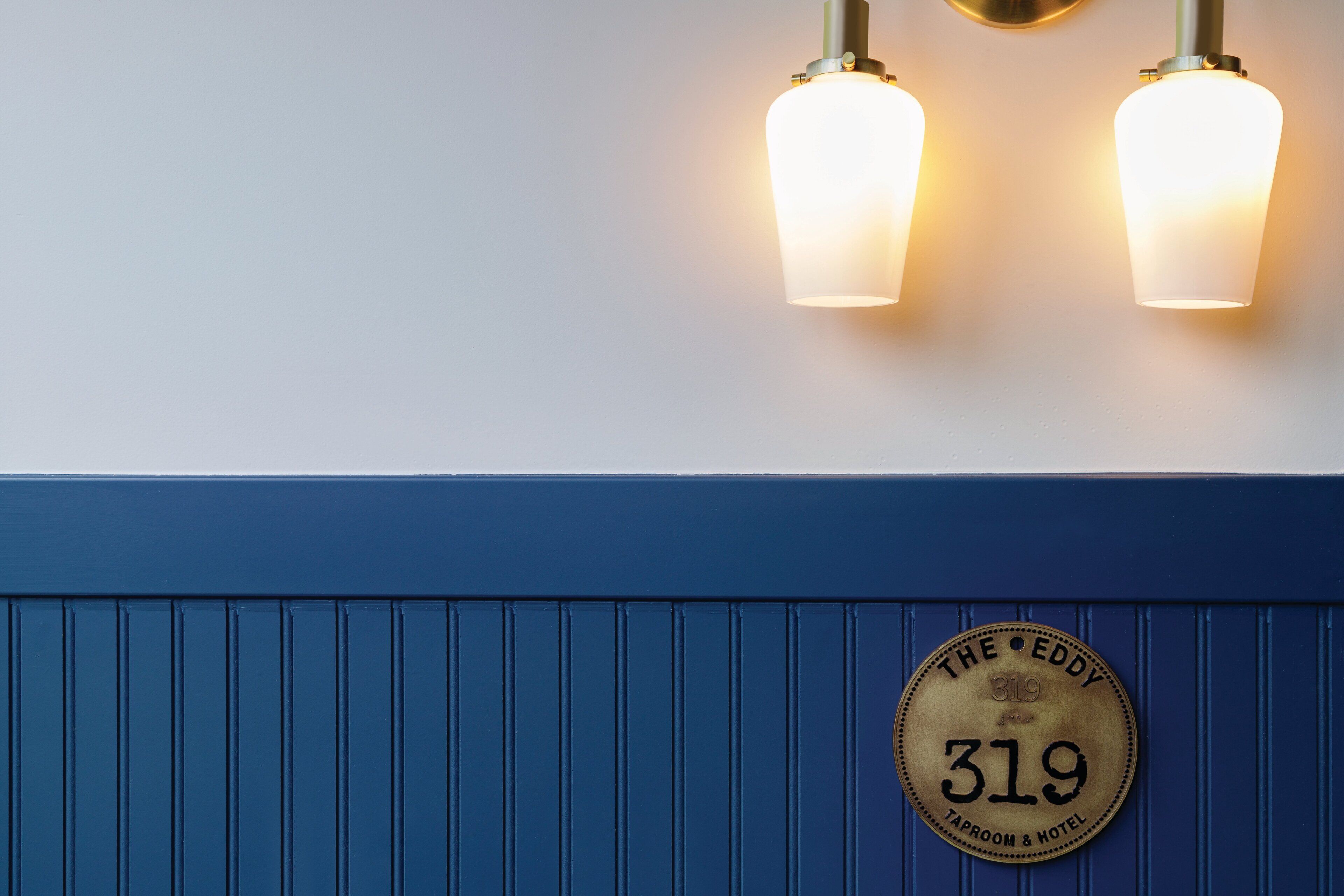 A wall with two wall-mounted lights and a plaque reading "The EDDY 319 TAPROOM & HOTEL".